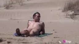 Nackter Mann liegt auf Handtuch im Sand.