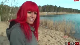 Lexy Roxx kniet mit freiem Hintern im Sand am See.